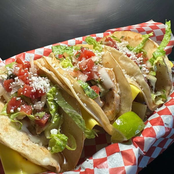 A basket of Hana Hou Restaurant's tacos with lettuce, tomatoes, cheese, and a lime wedge.