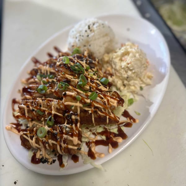 Crispy chicken drizzled with sauce, served with white rice and macaroni salad on a white plate.