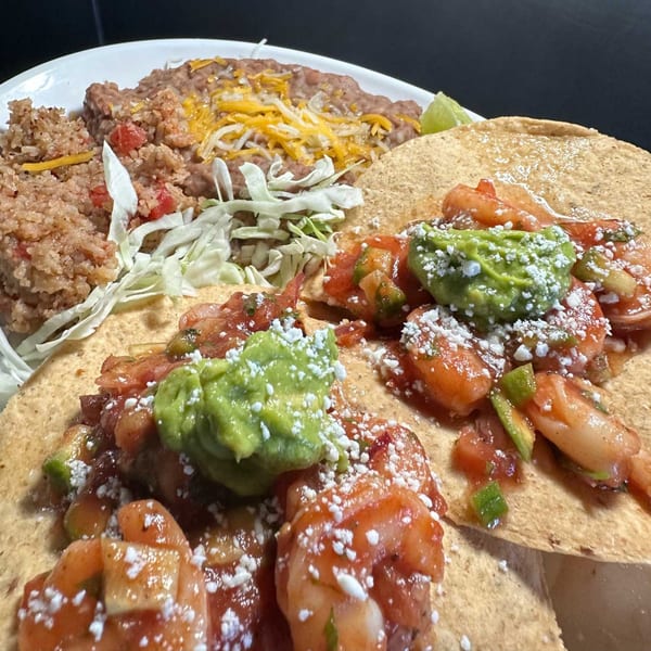 Shrimp tacos with guacamole, salsa, and cotija cheese, served with rice and refried beans.