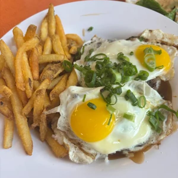 A diner plate with golden french fries and two fried eggs topped with green onions.